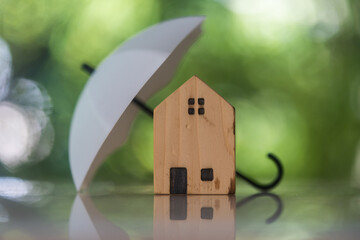 Wood house sheltered by umbrella with blur nature background. Insurance coverage concept. Home and home insurance concept