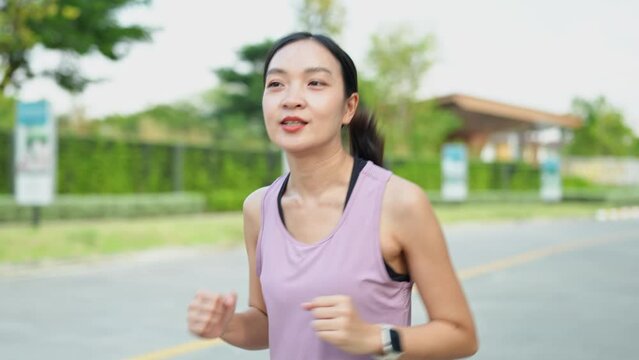 Female jogger, a young Asian woman wearing pink sportswear As she runs in the park in the morning sun. Soft sunlight. Health and outdoor activity concept.