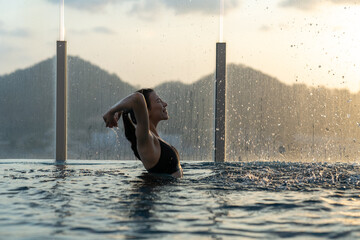 Beautiful white woman with black bikini relaxing in swimming pool at roof top hotel enjoying golden...