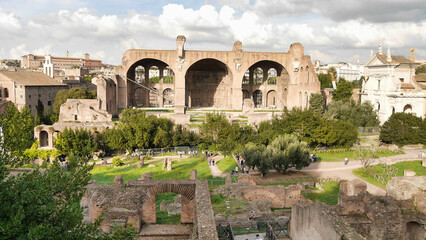 A view of the Roman Forum ruins, with the Basilica of Maxentius in the background, under a partly...