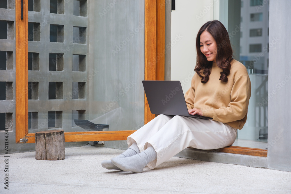 Wall mural Portrait image of a young woman working on laptop computer at home