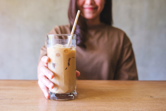 Closeup image of a young woman holding and serving a glass of iced coffee