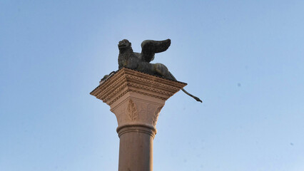 A sculpture of a winged lion on top of a tall column against a clear sky.