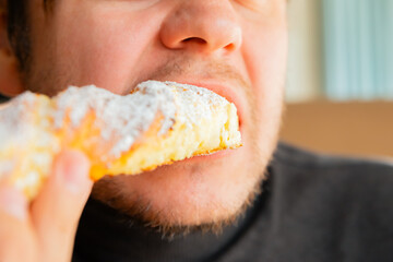 man eats freshly long curd baked sweet pastry bun in bakery cafe. Tasty sweet dessert close-up
