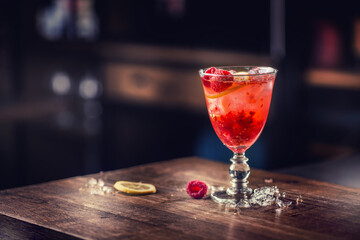 Alcoholic beverage with raspberries lemon and ice on bar counter in pub or restaurant