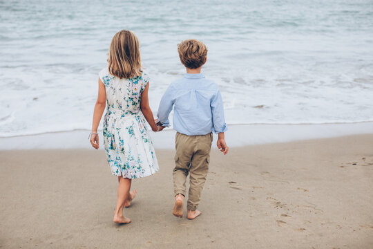 boy and girl walking and looking out at the ocean wearing khaki pants and a blue shirt and a blue floral dress