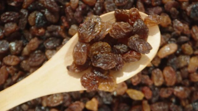 The camera slowly focuses on raisins in a wooden spoon. Close-up of a background of raisins.