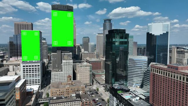 Skyline with buildings featuring green screens and tracking markers for visual effects. Aerial descending shot in modern American city against blue sky with puffy clouds.