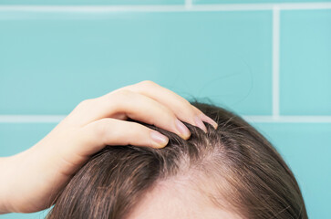 Fototapeta premium Woman touching her hair close-up on against background of mint tiles, hair loss concept.