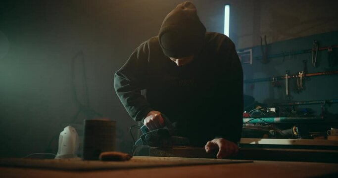Wide shot of skillful woodworker using planer to perfectly flatten planks in his workshop. Backlit slowmo shot