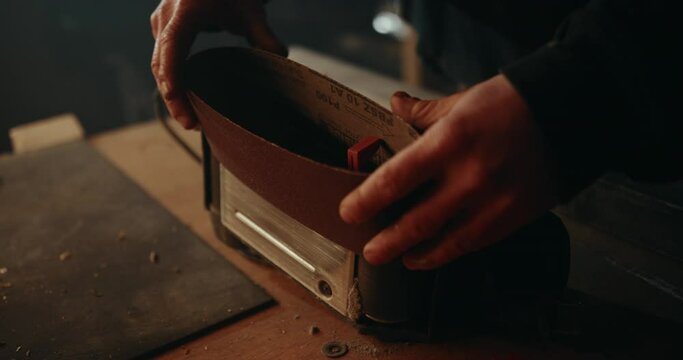 Putting a paper sanding belt on an electric belt grinder. Slow motion close up shot