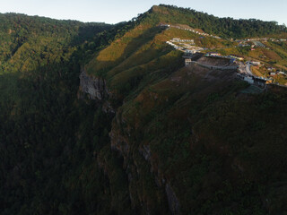 The early morning light reveals a village perched on the hillside of a mountainous region, with homes scattered along the winding path.