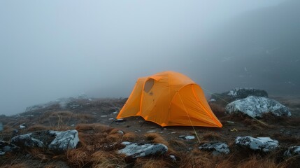 Orange tent on high mountain shrouded in fog