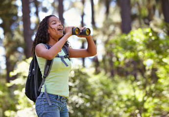 Happy girl, binoculars and nature with backpack for sightseeing, explore or outdoor vision. Young...