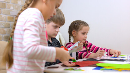 Cute little children cutting color paper with scissors at desk in kindergarten.