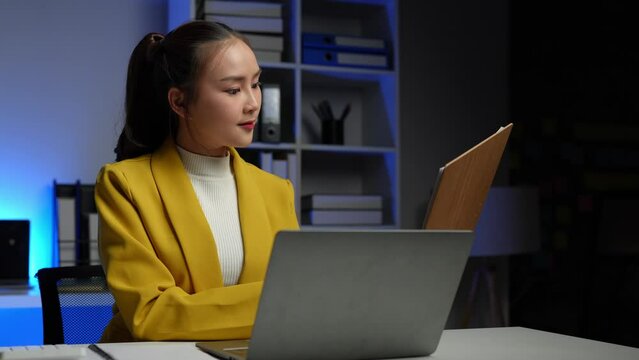 Cheerful Asian businesswoman using a laptop and writing on the charger to take notes. Analyzing finances, online markets, and taxes and happily collecting thoughts and ideas in her office.