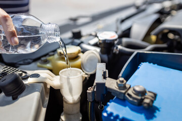 Close up,Pouring clean water from plastic bottle into the windshield washer fluid tank of a car,filling the windshield washer fluid,check liquid level in engine room,service and maintenance concept