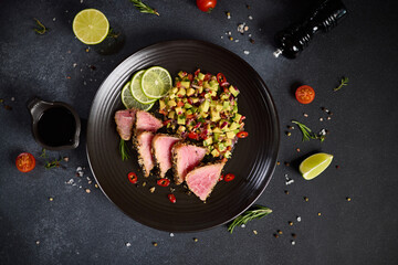 Sliced Organic grilled Tuna fillet covered with sesame seeds and salsa on black ceramic plate