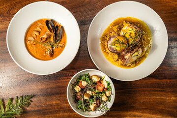 Exquisite seafood cream, salad and main course. Hotel restaurant food. Meals on wooden table.