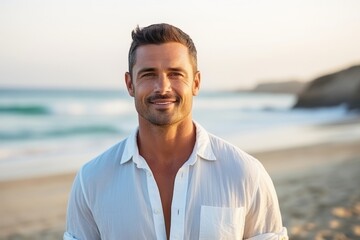 Portrait of handsome man standing on beach with hand in pocket smiling at camera