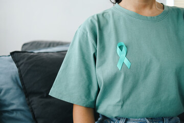 Close up Teal Awareness Ribbon on Teal T-Shirt to Support Cervical Cancer Survivor. Ovarian Cancer Month.  - obrazy, fototapety, plakaty