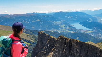 Hiker woman on idyllic hiking trail on alpine meadow with scenic view of lake Millstatt seen from mountain peak Boese Nase, Ankogel Group, Carinthia, Austria. Remote landscape. Austrian Alps in summer