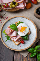 Fried eggs for breakfast with a ham sandwich. Toast bread, greens, olives are on the table.