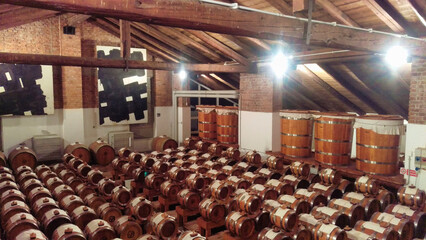 Rows of wooden wine barrels in a cellar, illuminated by warm overhead lights, evoke a sense of...