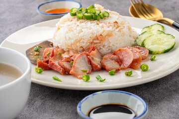 Barbecued red pork in sauce with rice on a white plate, accompanied by soup and dipping sauce, is...