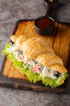 Croissant sandwich with salad made from chicken, grapes, onions, celery, dressed with mayonnaise close-up on a wooden board on the table. Vertical