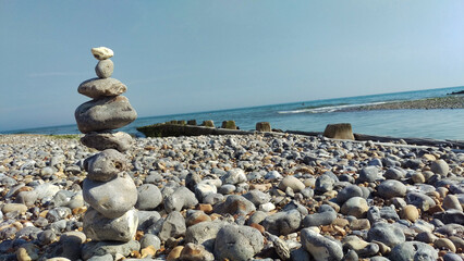 Rocky beach with stacked stones in the foreground and white cliffs in the background under a clear...