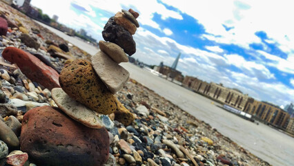 A creative arrangement of stacked stones with a cityscape background under a cloudy sky.