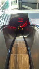 Dimly lit escalator descending into a red-lit underground station.