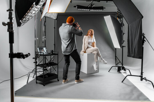 Man photographing woman sitting on cube in photo studio