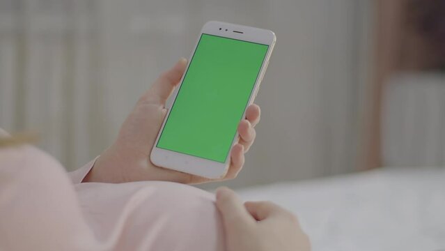 Smartphone with green chroma key screen hold by Pregnant woman, show ease of technology use in casual setting. Perfect for screen replacement, graphic designers to superimpose their own content.