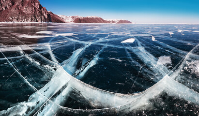 Blue transparent cracked ice and rocks on Baikal lake, Siberia, Russia.