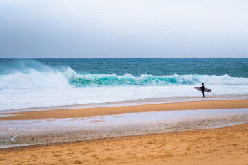 Surfer with surfboard waiting for the big wave. Atlantic ocean, Nazare, Portugal