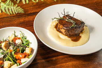 Exquisite steak on melted cheese with delicious salad in a hotel restaurant. Main course and side dish.