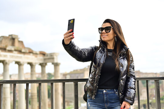 Rome,Italy, Young beautiful woman  near The Fori Imperiali enjoying the city at Rome during language vacation. Using a mobile phone taking a pictures.Concept of Italian gastronomy and travel