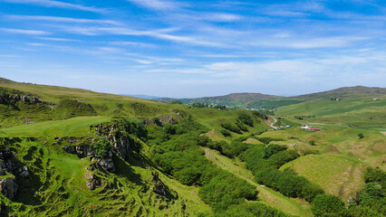 Fototapeta na wymiar Lush green valley with rolling hills under a vast blue sky dotted with a few clouds.