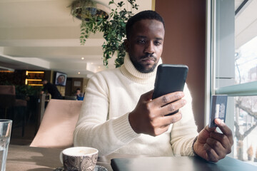 Young black man online shopping with a credit card and mobile phone in hands 