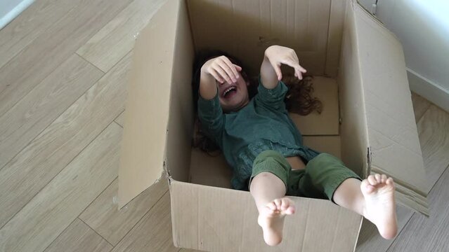 Child laying into a big box and playing with legs and hands, preparing to move house. High quality FullHD footage