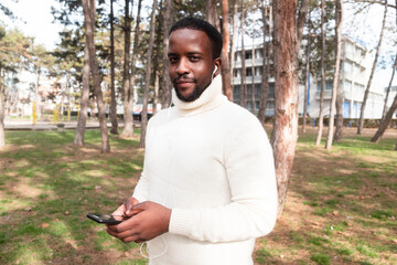 Young black man yuppie hipster in a park using a mobile phone and smiles