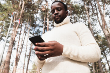 Young black man yuppie hipster in a park using a mobile phone