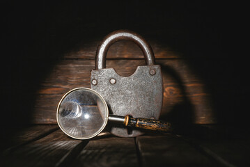 Old barn padlock and magnifying glass on the wooden desk table background close up. Secret...