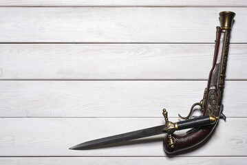 Vintage retro style dagger sword and musket gun on the white wooden flat lay table background with copy space. Pirate table.