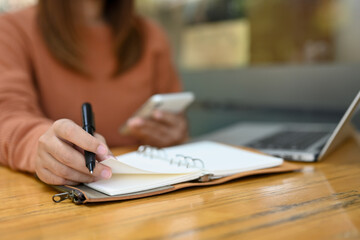 Woman using mobile phone and writing important things on notepad