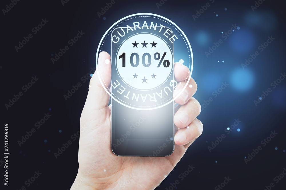 Poster hand holding smartphone displaying 100 percent guarantee badge, assurance and quality concept on dar
