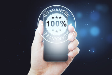 Hand holding smartphone displaying 100 percent guarantee badge, assurance and quality concept on...