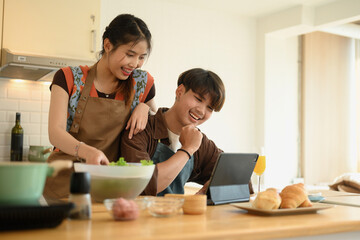 Happy young couple preparing food in kitchen and reading recipe on digital tablet